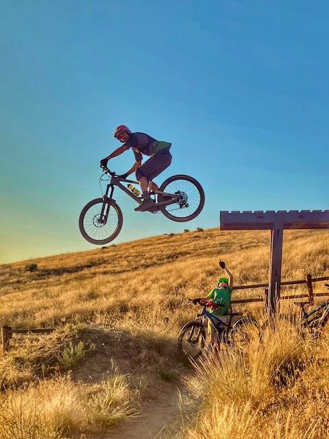 A mountain biker in the air off a jump on a dry grass hillside