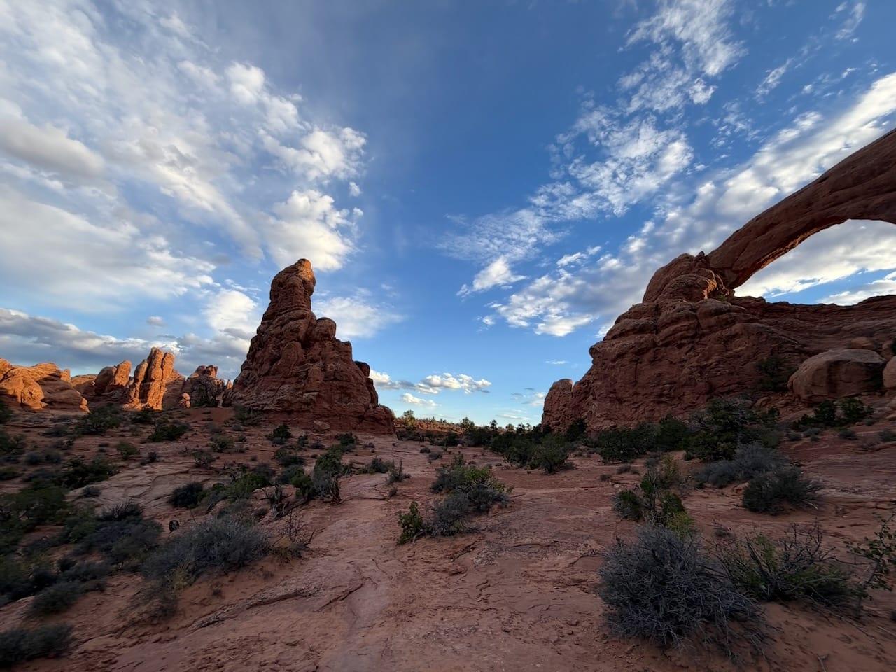 A red rock arch and spire in the desert under a wide sky
