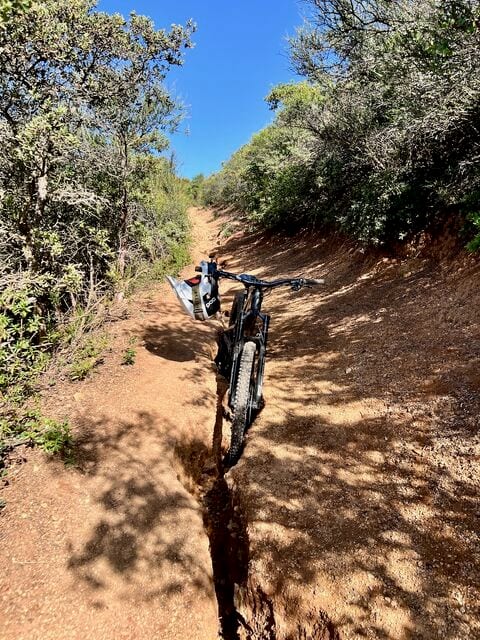 A mountain bike standing in a deep rut cut by erosion down the middle of a dirt trail