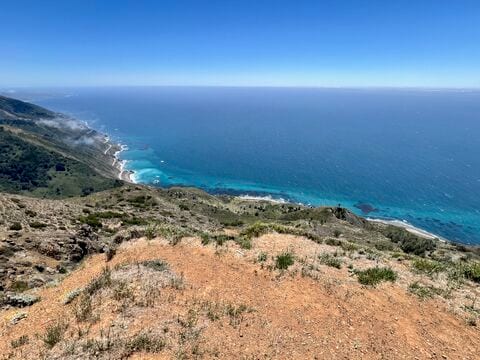 The Big Sur coastline seen from a high, dry ridge, with blue-green water below and fog along the hills